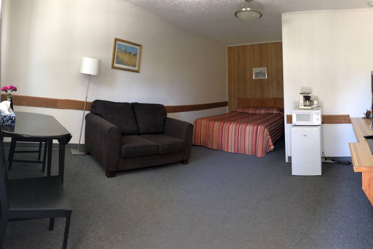 Ein Hotelzimmer mit einem Bett, einer Couch, einem Schreibtisch mit Stuhl, einer Mikrowelle und einem Fernseher.