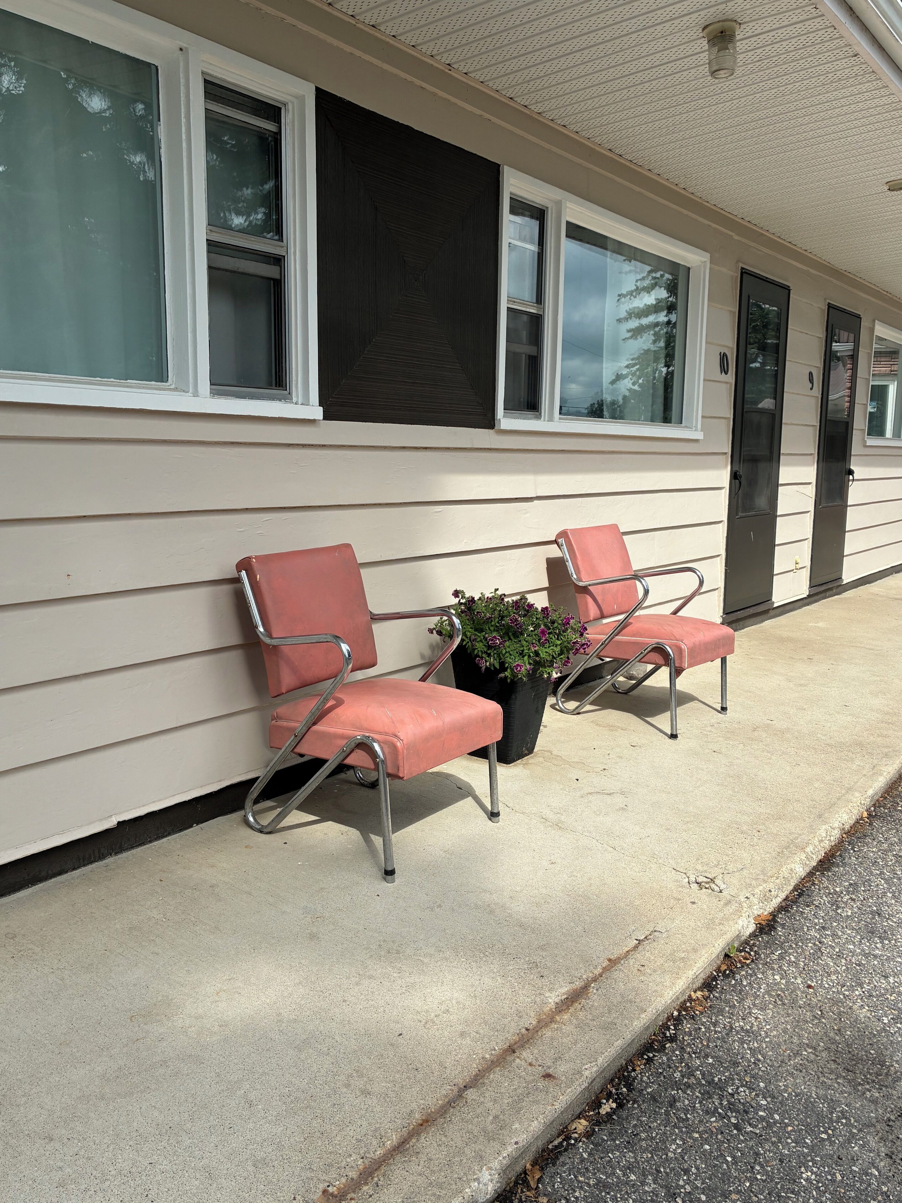 A motel with two red chairs and a potted plant on the sidewalk.