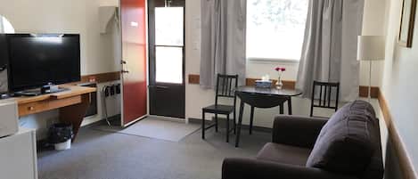 A compact hotel room with a TV, a desk, a dining table, and a sofa.
