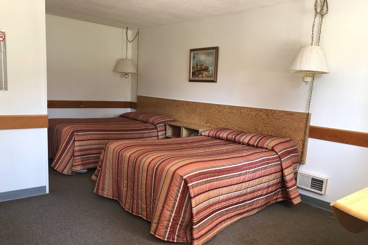 Ein Hotelzimmer mit zwei Betten, einem hölzernen Kopfteil, einem Gemälde an der Wand und einer Pendelleuchte.