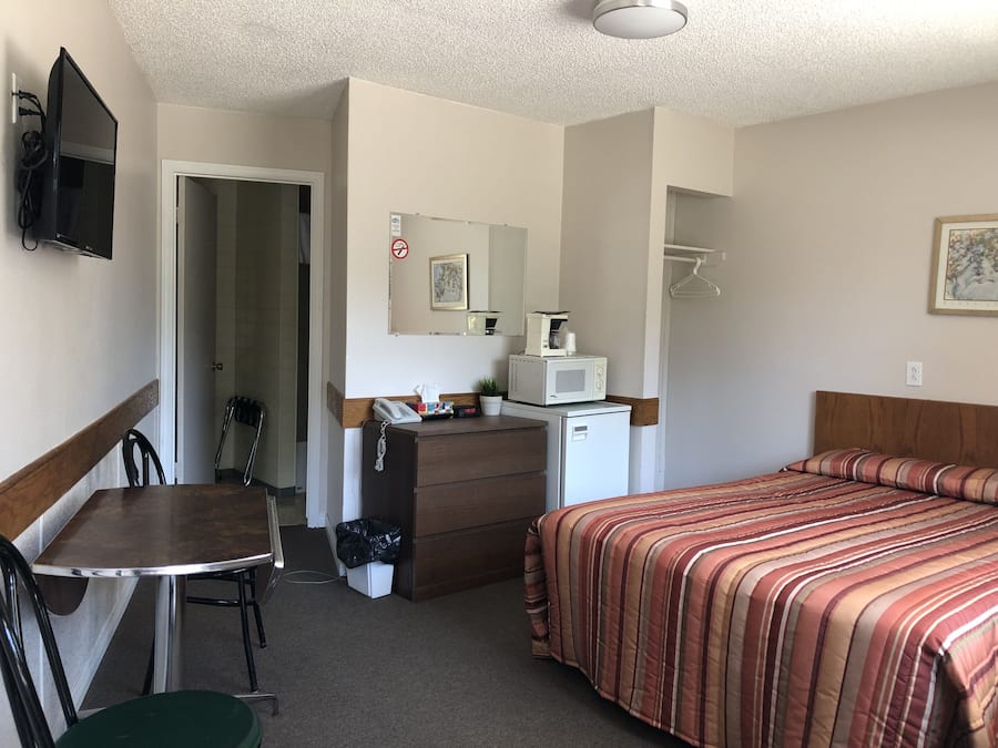 A hotel room with a bed, a desk with a chair, a dresser, a microwave, and a television.