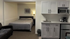 A hotel room with a bed, a desk, a microwave, a coffee maker, and a trash can. - Yellow Quill Motel (Portage La Prairie)