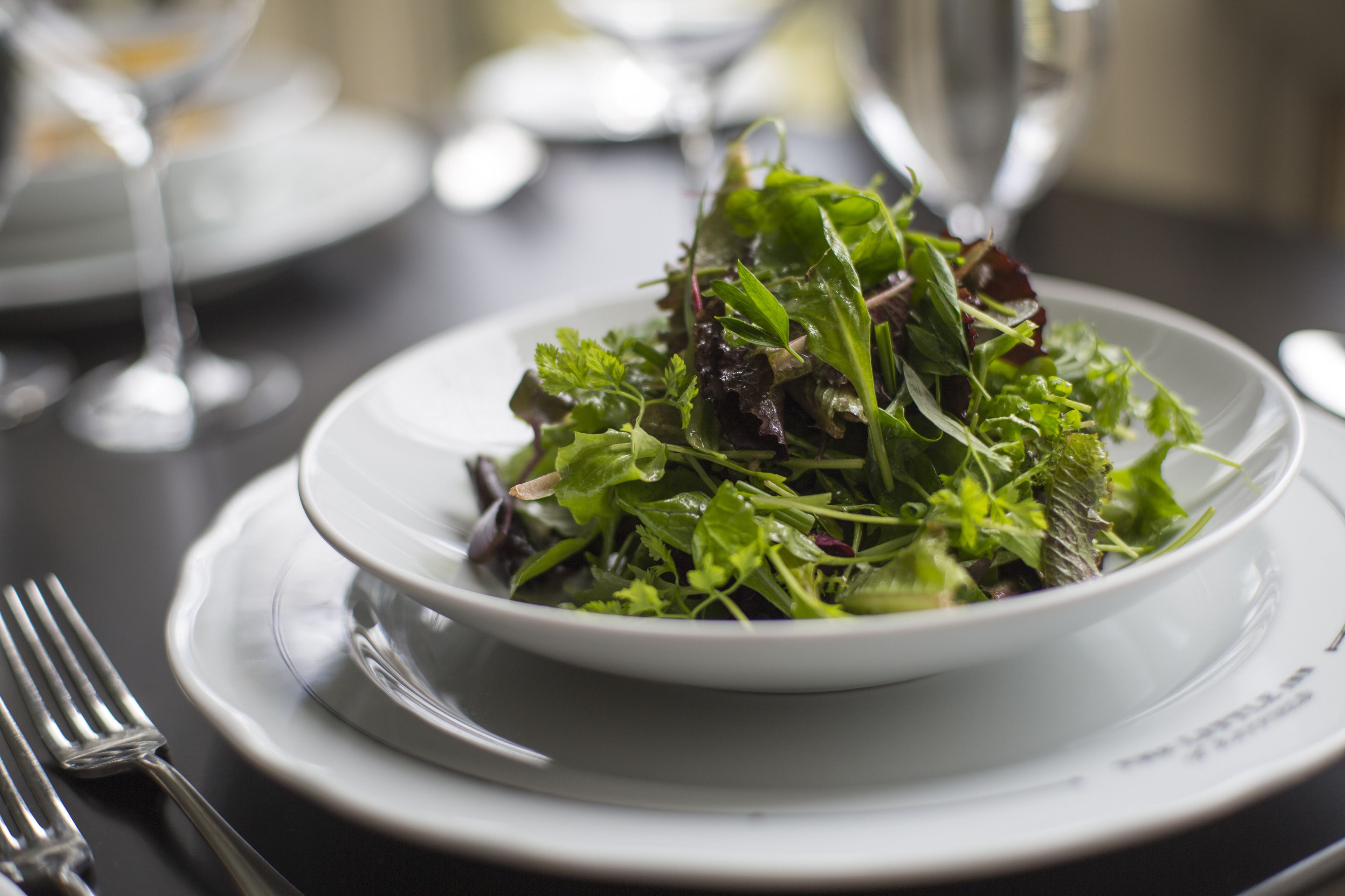 Un plato blanco con una ensalada sobre una mesa oscura.