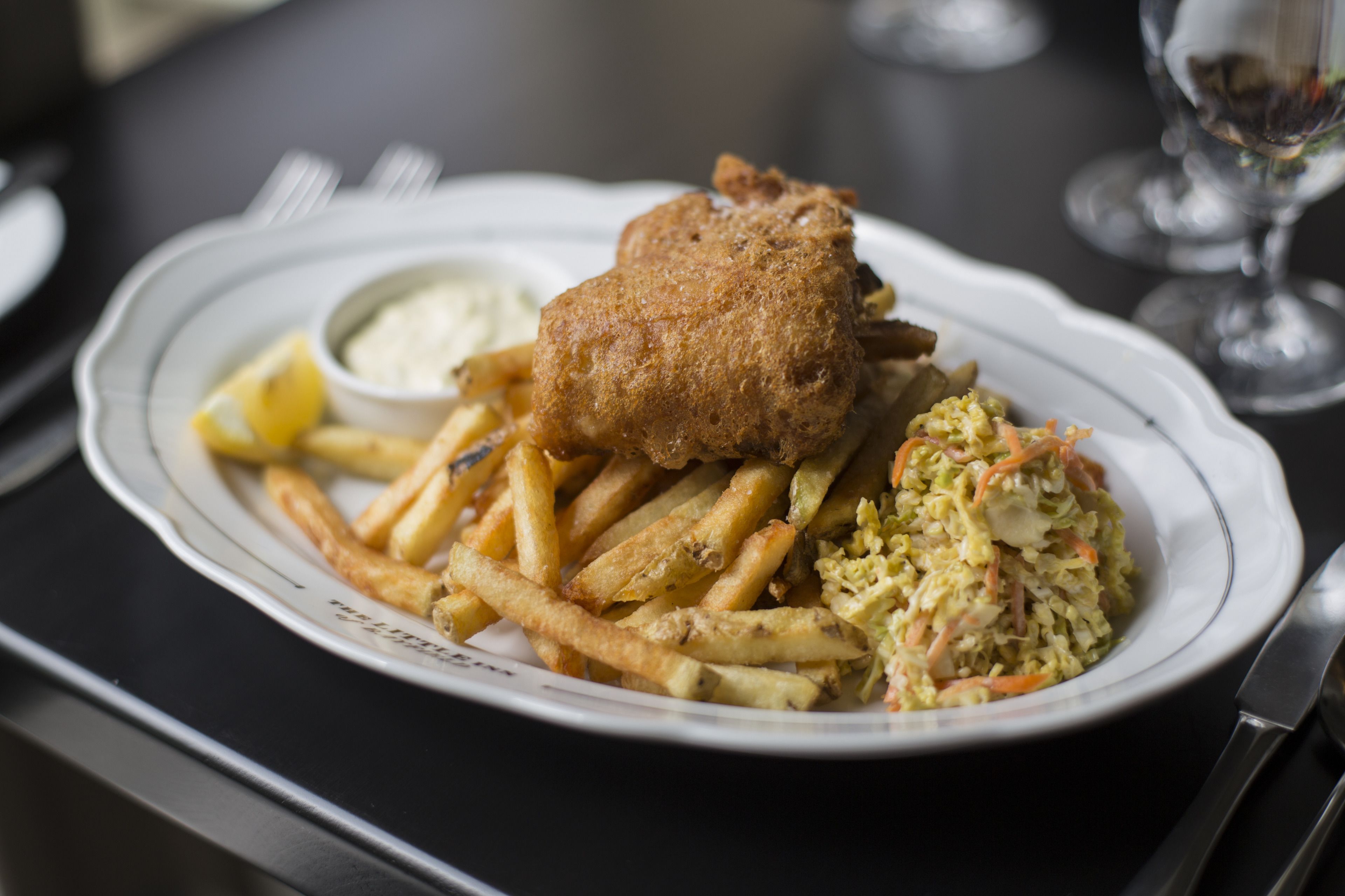 Un plato de pescado con patatas fritas y ensalada de col.