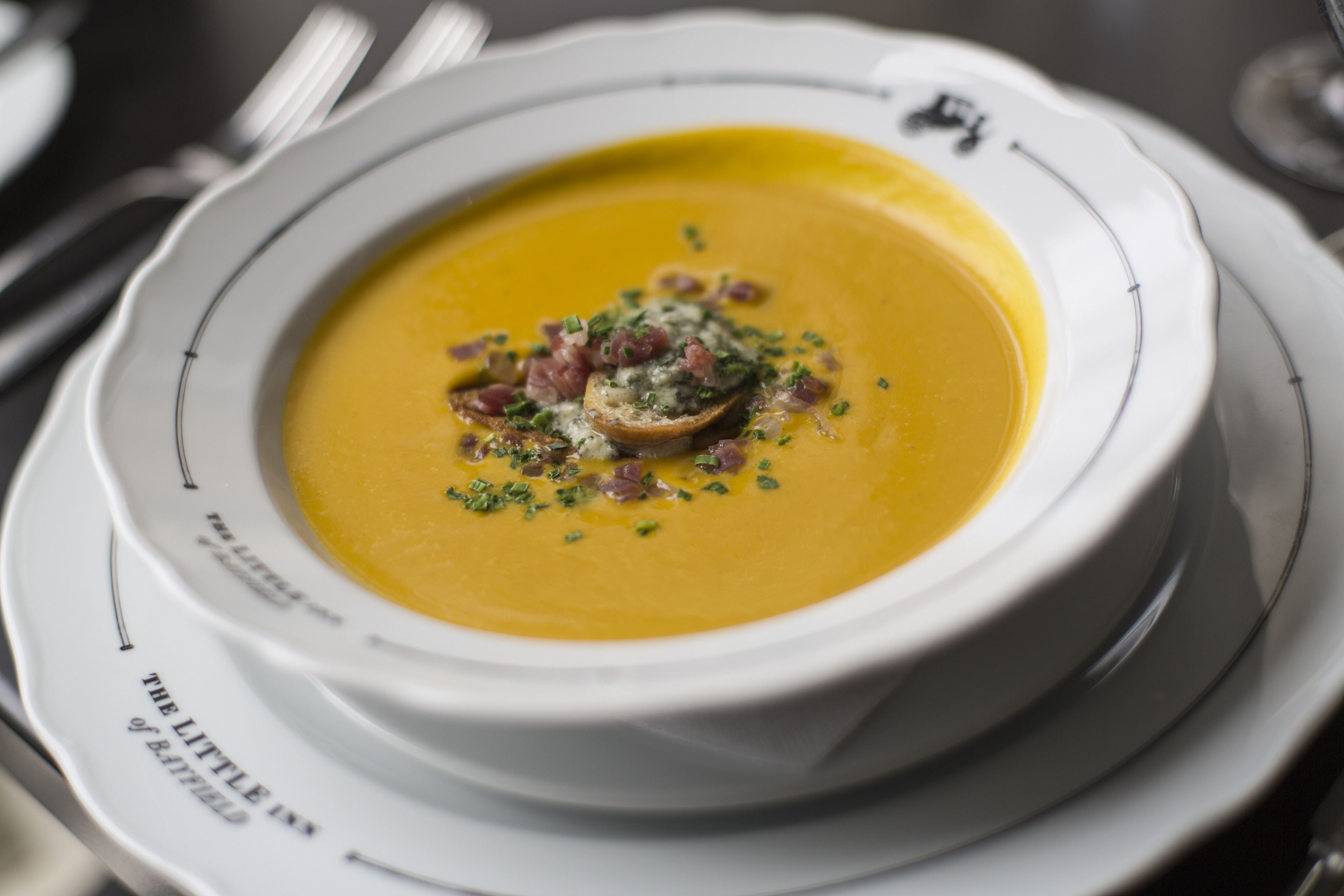 A bowl of soup with garnishes on a plate.