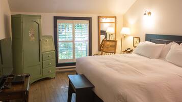 Une chambre d’hôtel avec un grand lit, un bureau en bois, une commode verte, une chaise et une fenêtre donnant sur un paysage verdoyant.
