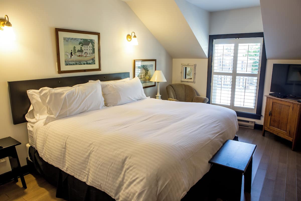 A large bed with white linens, a nightstand, a chair, a television, and framed artwork on the walls.