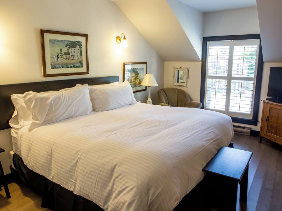 A large bed with white linens, a nightstand, a chair, a television, and framed artwork on the walls.