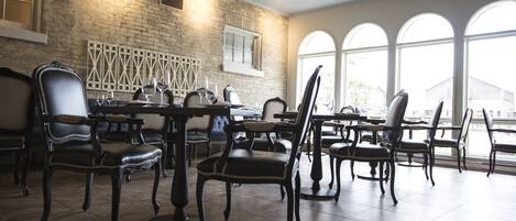 A spacious dining area with high-backed chairs, a brick wall, and large windows.