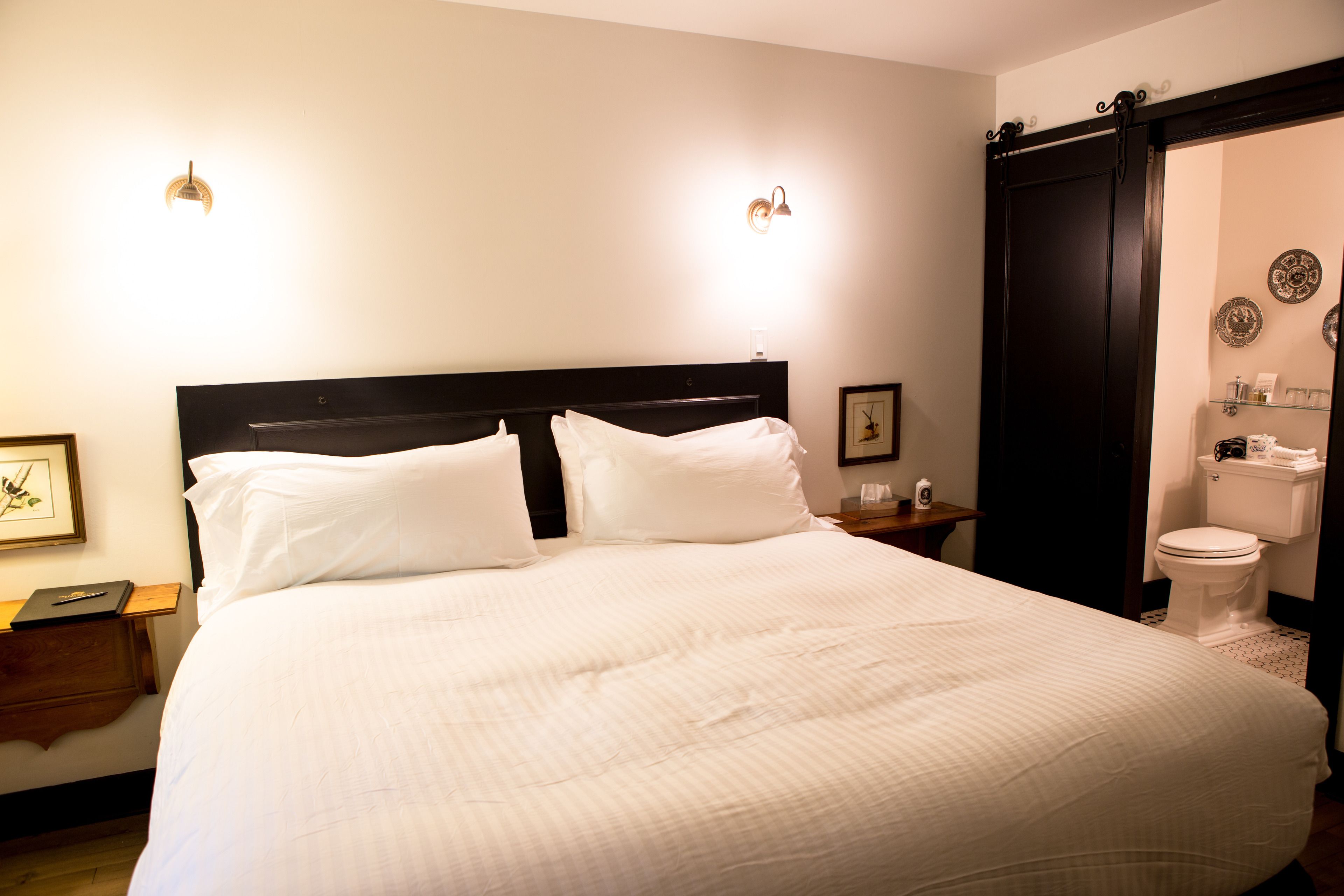 Een net opgemaakt bed met witte lakens, een houten hoofdbord en twee bedlampjes.