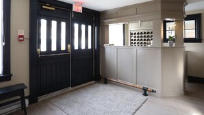 A hallway with a black double door, a white wall with a bulletin board, and a small bench. - The Little Inn of Bayfield (Bluewater)