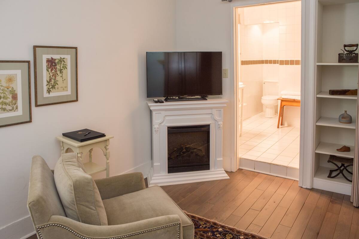 A living room with a fireplace, a television on a mantel, and a door leading to a bathroom.