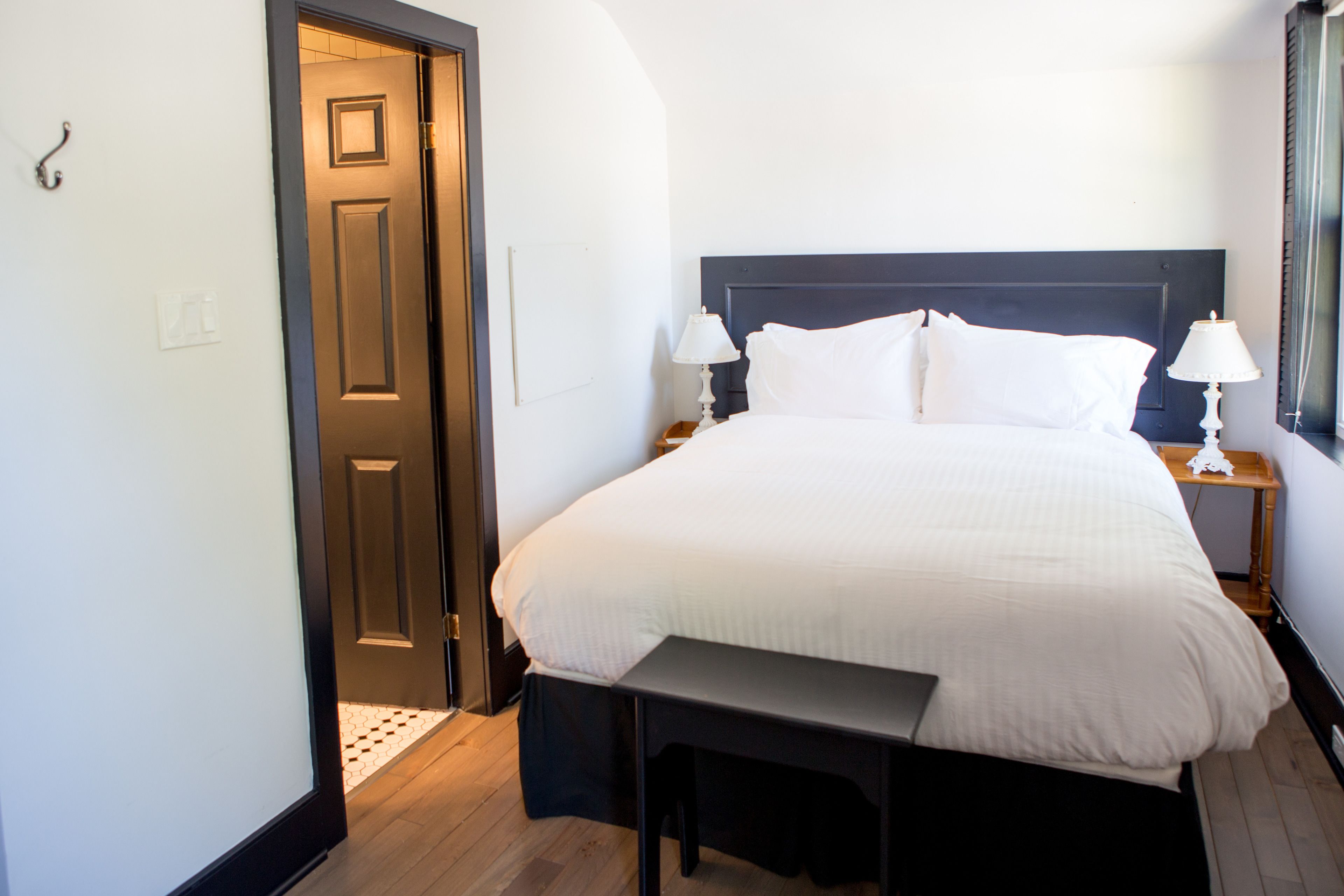 A neatly made bed with white linens, a dark headboard, and two bedside lamps.