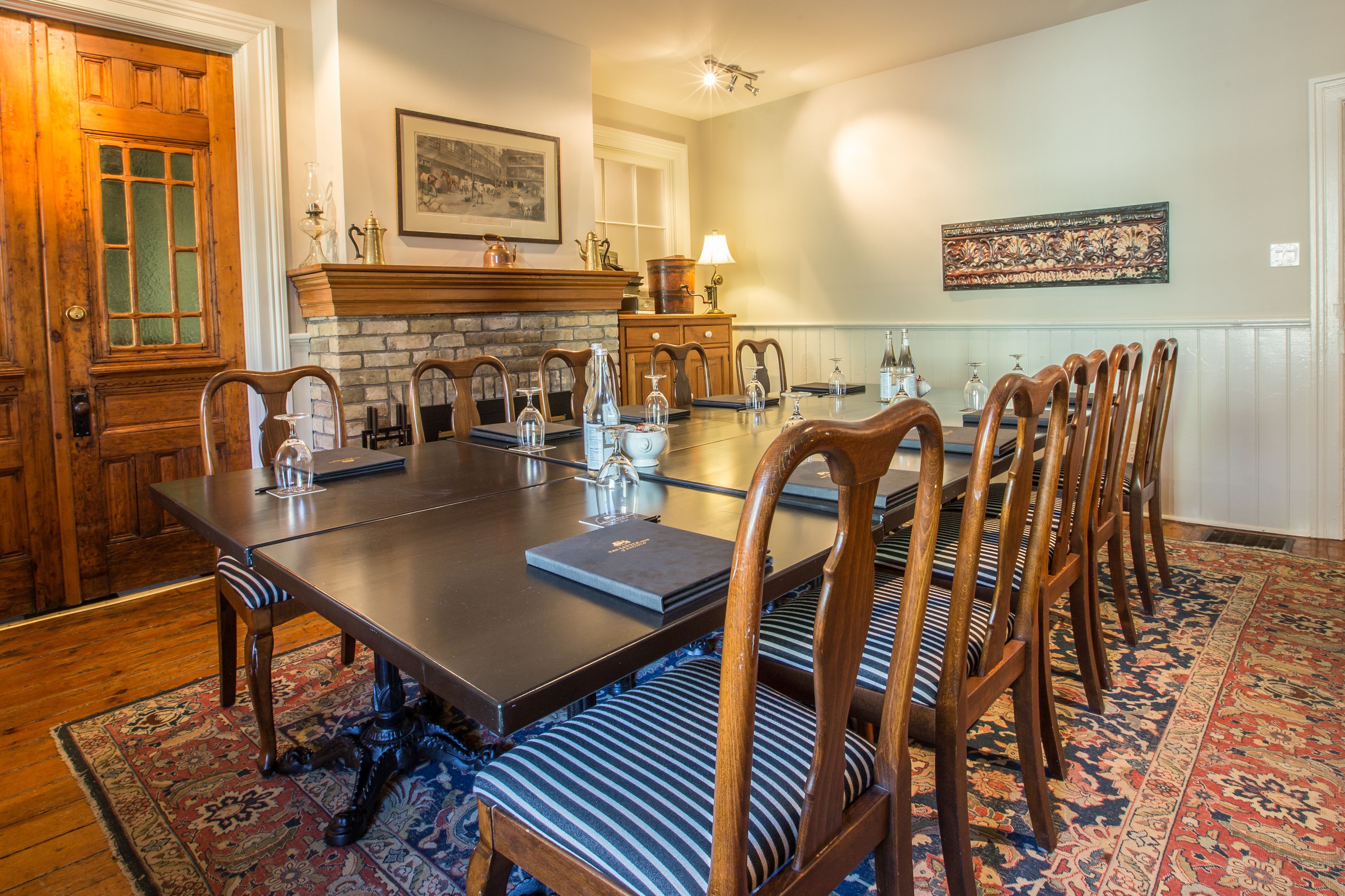 A dining room with a long table, wooden chairs, a fireplace, and a patterned rug.