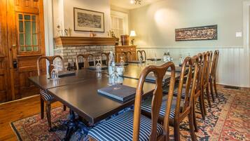 A dining room with a long table, wooden chairs, a fireplace, and a patterned rug.