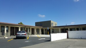 Ein Motel mit Parkplatz, einem Auto und einem Gebäude mit vielen Fenstern und Eingängen.