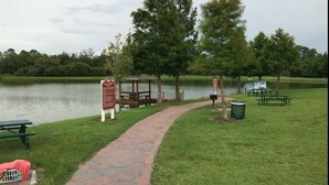A paved pathway leading to a gazebo by a lake, picnic tables, and a trash bin. - Villas at Seven Dwarf by FunQuest (Kissimmee)