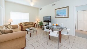 A living room with a sofa, a coffee table, a TV, and a dining area with chairs and a table. - Villas at Seven Dwarf by FunQuest (Kissimmee)