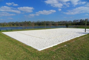 Een volleybalveld met een net, omgeven door gras en een meer op de achtergrond.