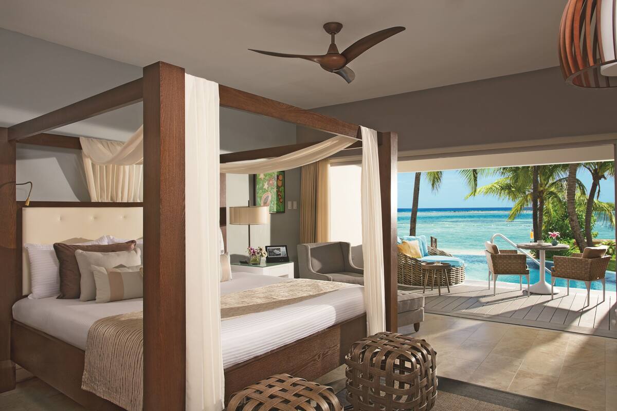 Ein Bett mit Baldachin und Meerblick, ein Deckenventilator und ein Balkon mit Sitzgelegenheit.
