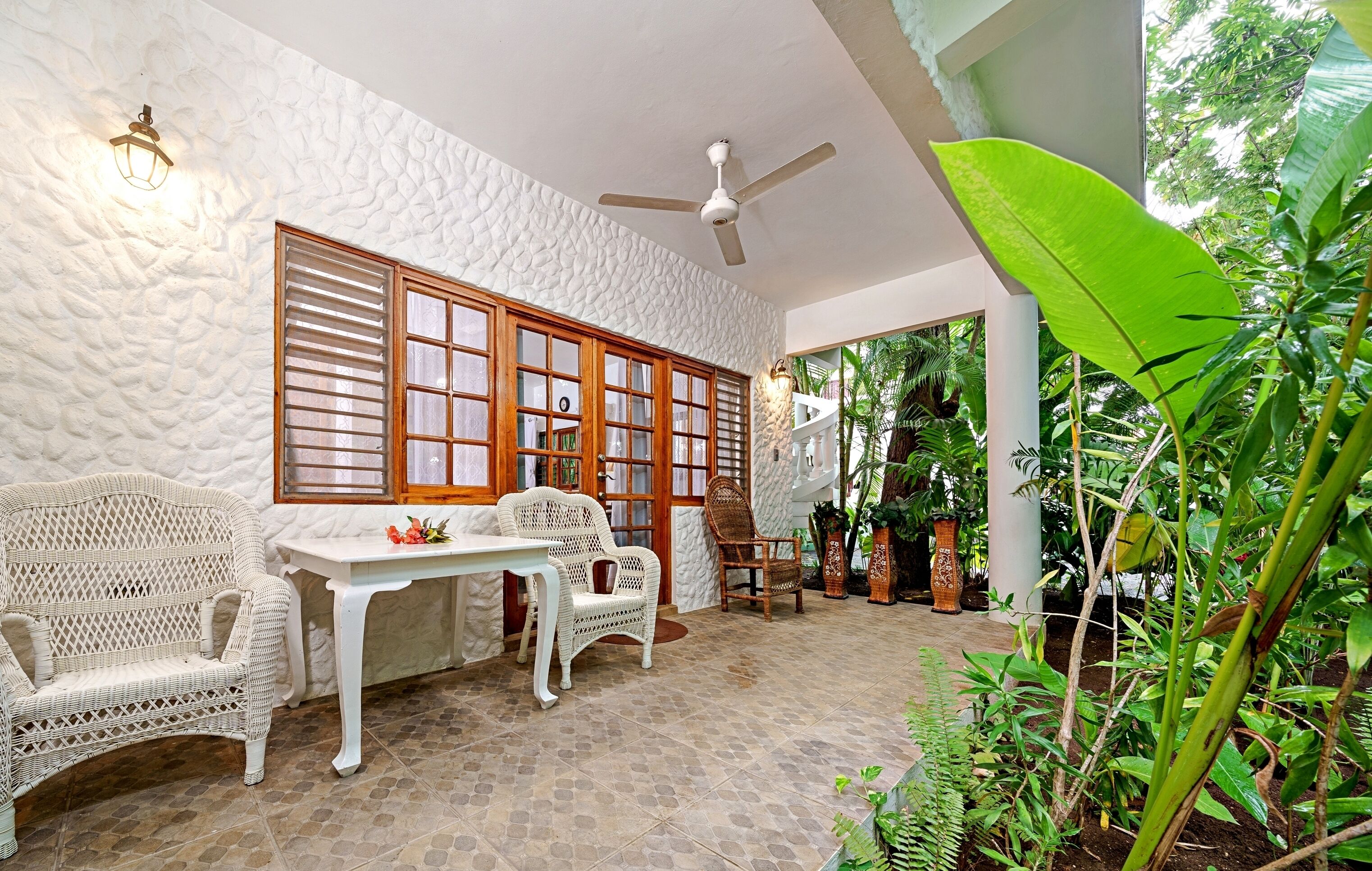 A room with a white textured wall, a ceiling fan, a wooden door with glass panels, wicker furniture, and a potted plant.