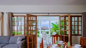 Ein Zimmer mit grauem Sofa, einem Holzespeisetisch, der mit weißen Tellern und Schüsseln gedeckt ist, und Blick auf üppiges Grün draußen.