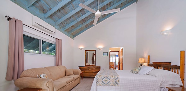 Une chambre à coucher comprenant un lit, un canapé, une commode, un ventilateur de plafond et une fenêtre avec des rideaux.