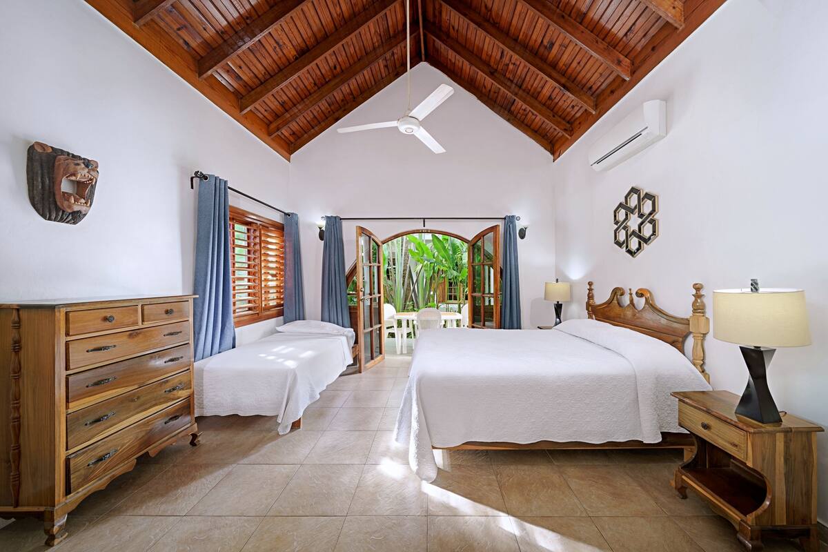 Una habitación con dos camas, muebles de madera, ventilador de techo y vistas al exterior.