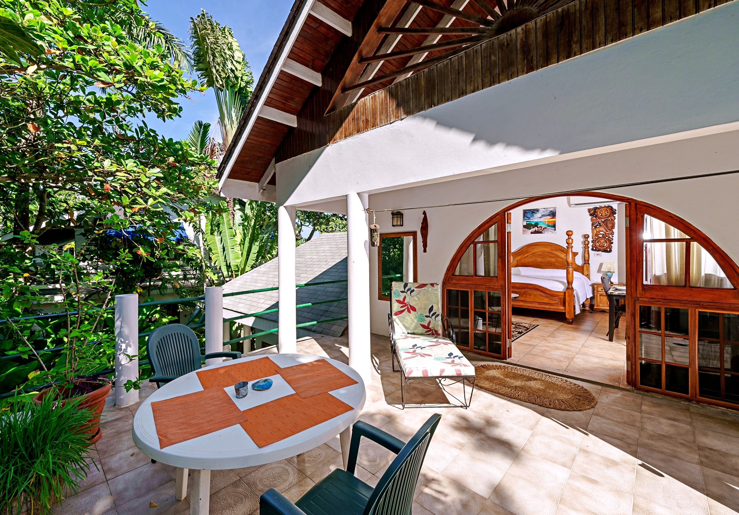 A patio with a round table and chairs, a bed with a wooden headboard, and a view of the garden.