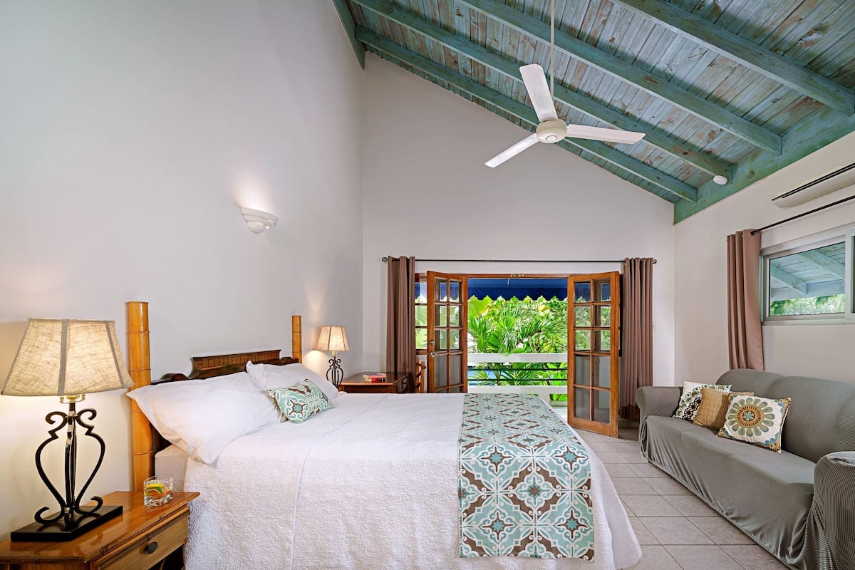 Habitación de hotel con cama, sofá, ventilador de techo y vistas a zonas verdes.