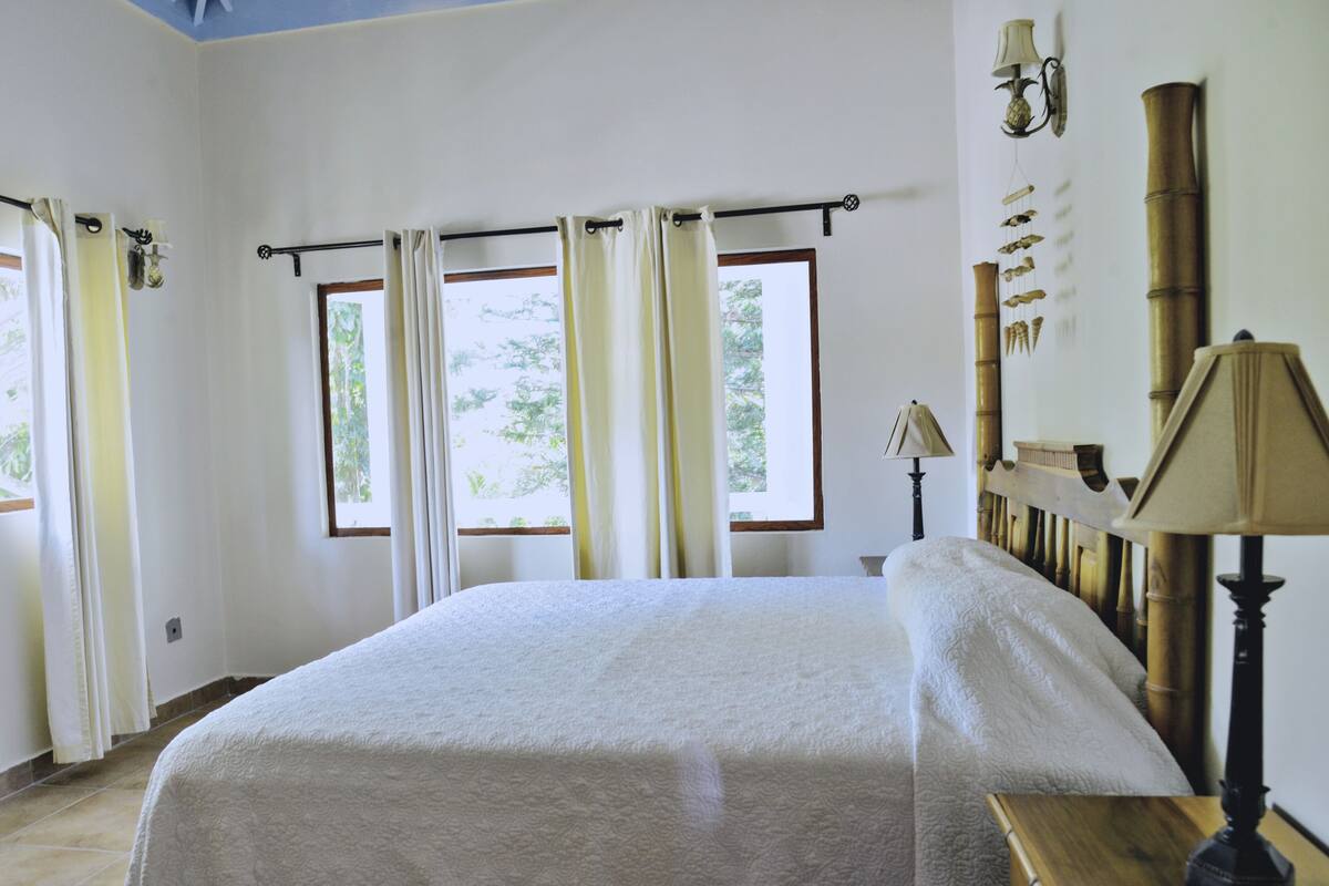 Un dormitorio con una cama grande, una mesita de noche de madera, una lámpara y un estante en la pared con objetos decorativos.
