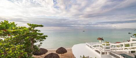 A beach view with a white building, thatched umbrellas, and a clear sky.