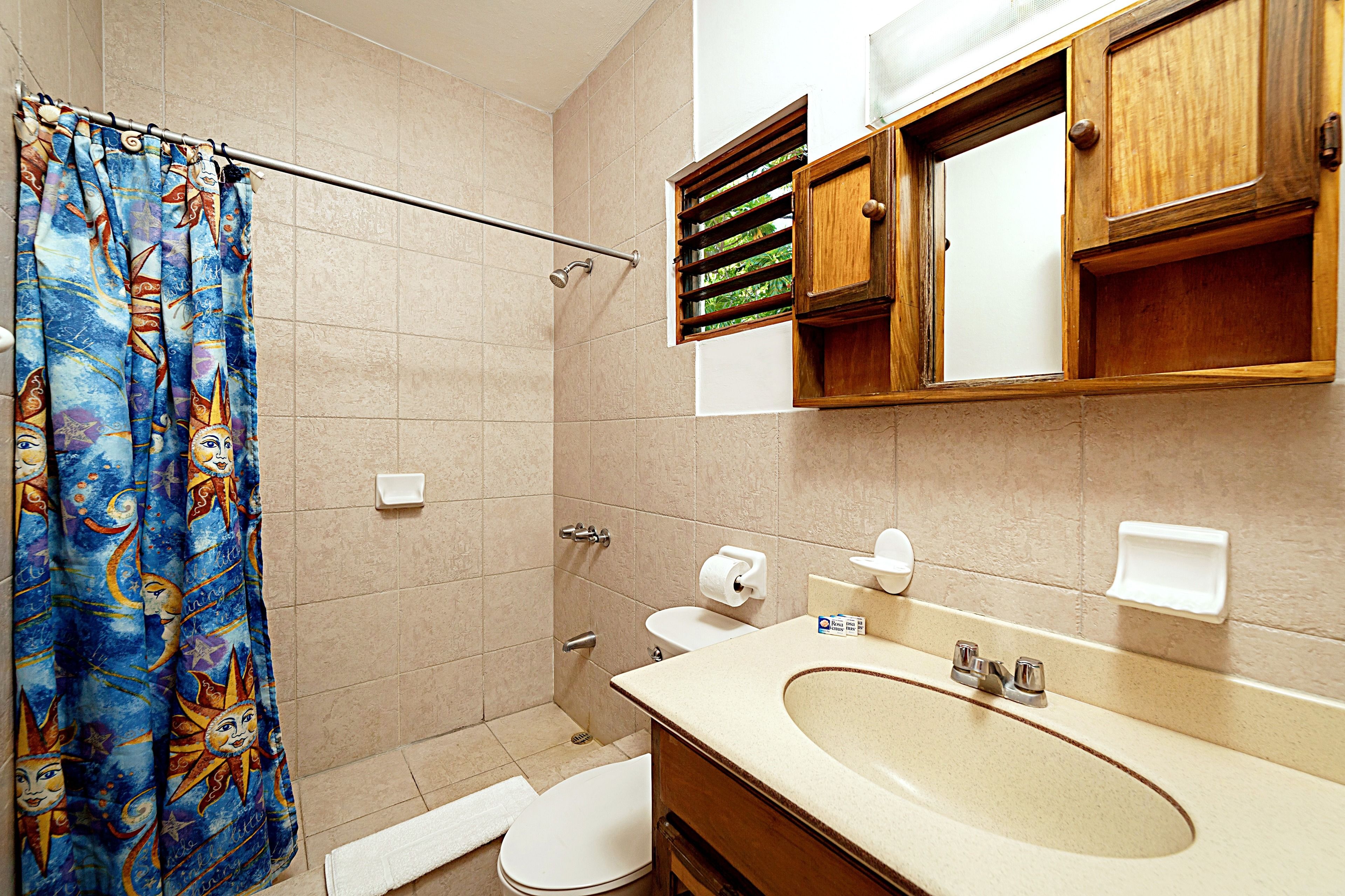 A bathroom with a shower curtain, toilet, sink, and wooden cabinets.