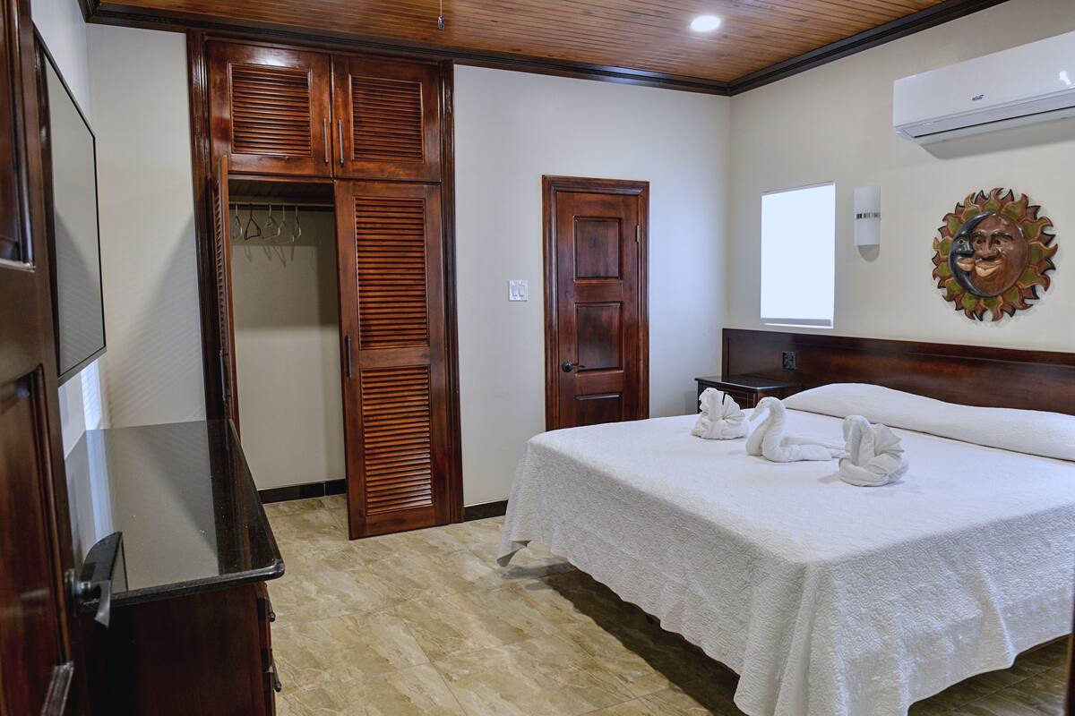 Habitación de hotel con cama, armario de madera, espejo y aire acondicionado instalado en la pared.