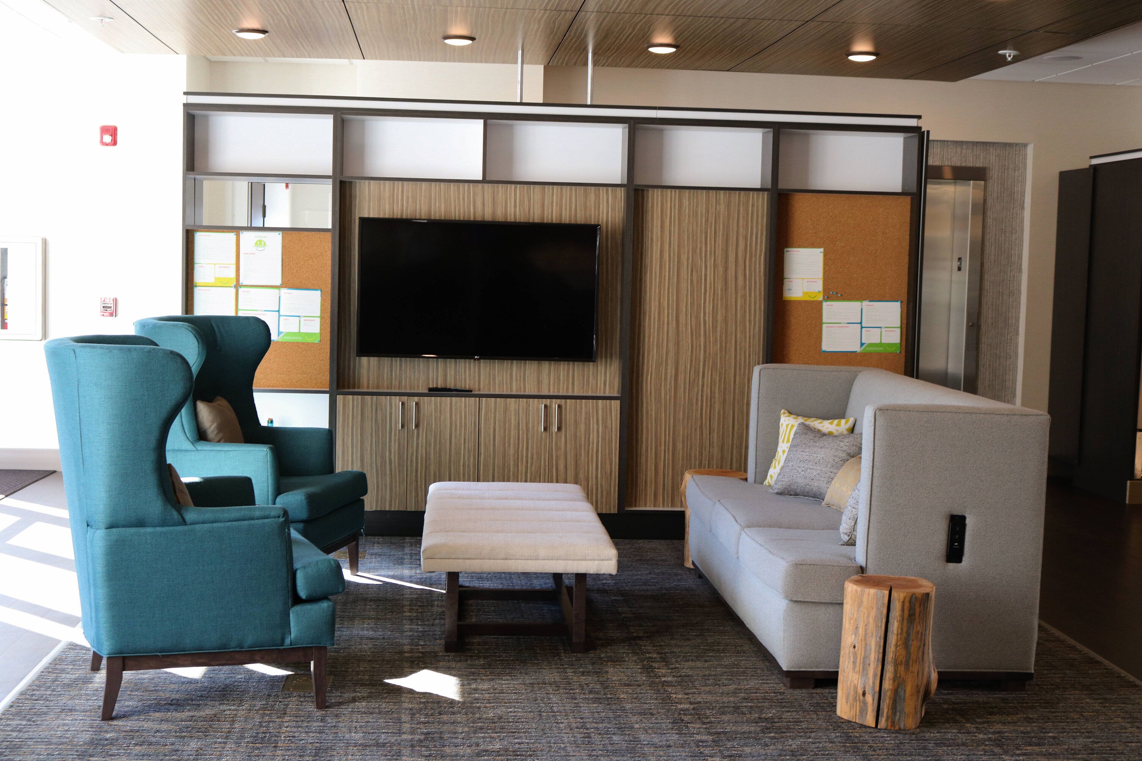 A modern lounge area with seating, a flat-screen TV, and bulletin boards.