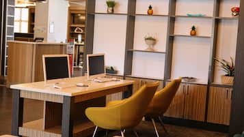 A reception area with a desk, two chairs, a computer, and a plant on shelves.