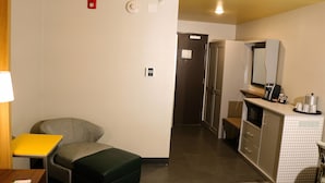 A compact hotel room with a kitchenette, a small seating area, and a door leading to another room. - Holiday Inn Jonesboro by IHG (Jonesboro)