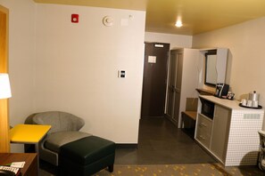 Une chambre d’hôtel compacte dotée d’une kitchenette, d’un petit coin salon et d’une porte donnant sur une autre pièce.