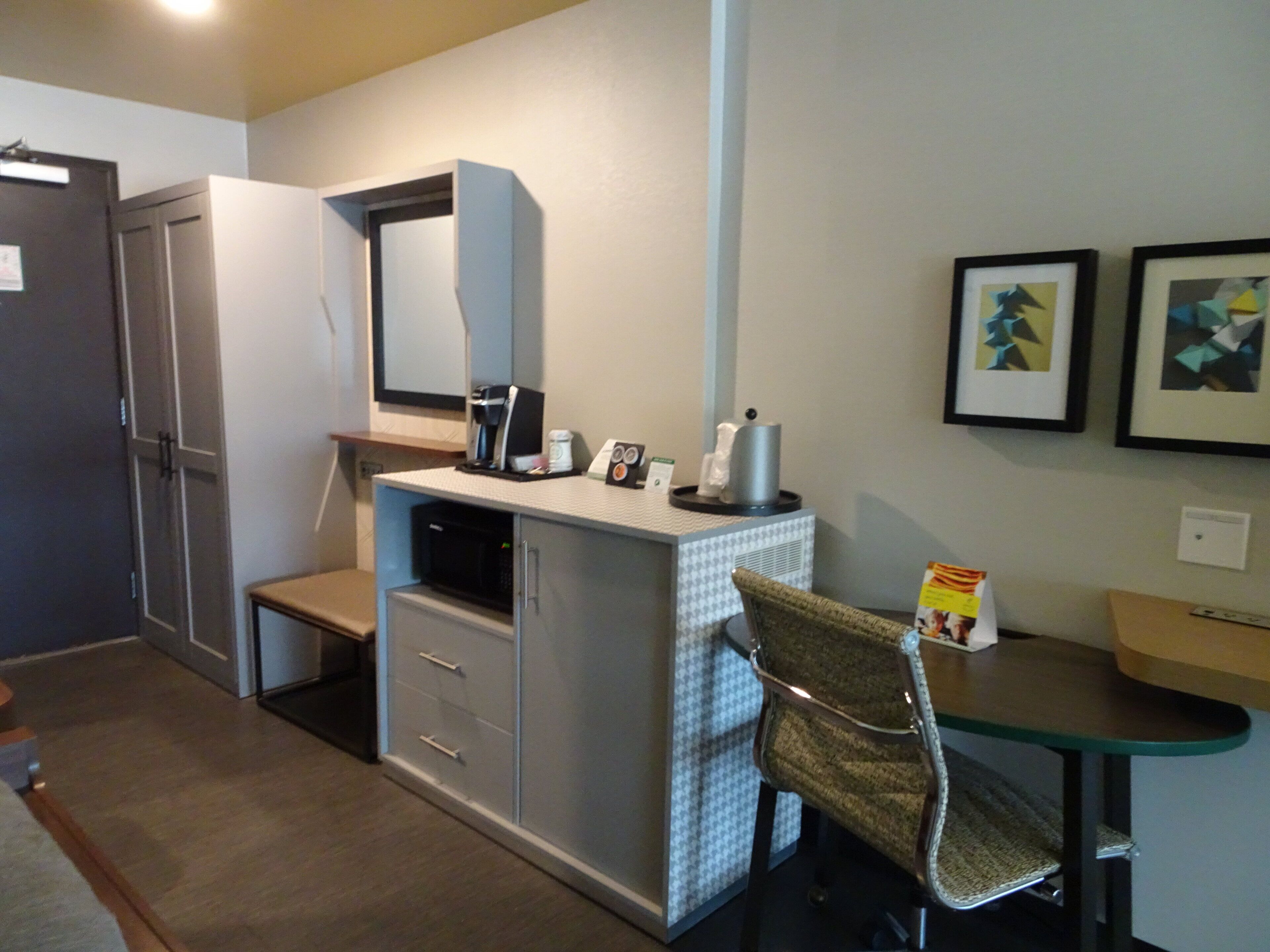 A compact room with a kitchenette, a microwave, a coffee maker, a chair, and a desk.