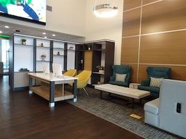 Um lobby moderno com balcão de recepção, duas poltronas, um sofá e uma tela de televisão.