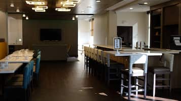Restaurante com várias mesas e cadeiras, um balcão com um letreiro e uma televisão na parede.