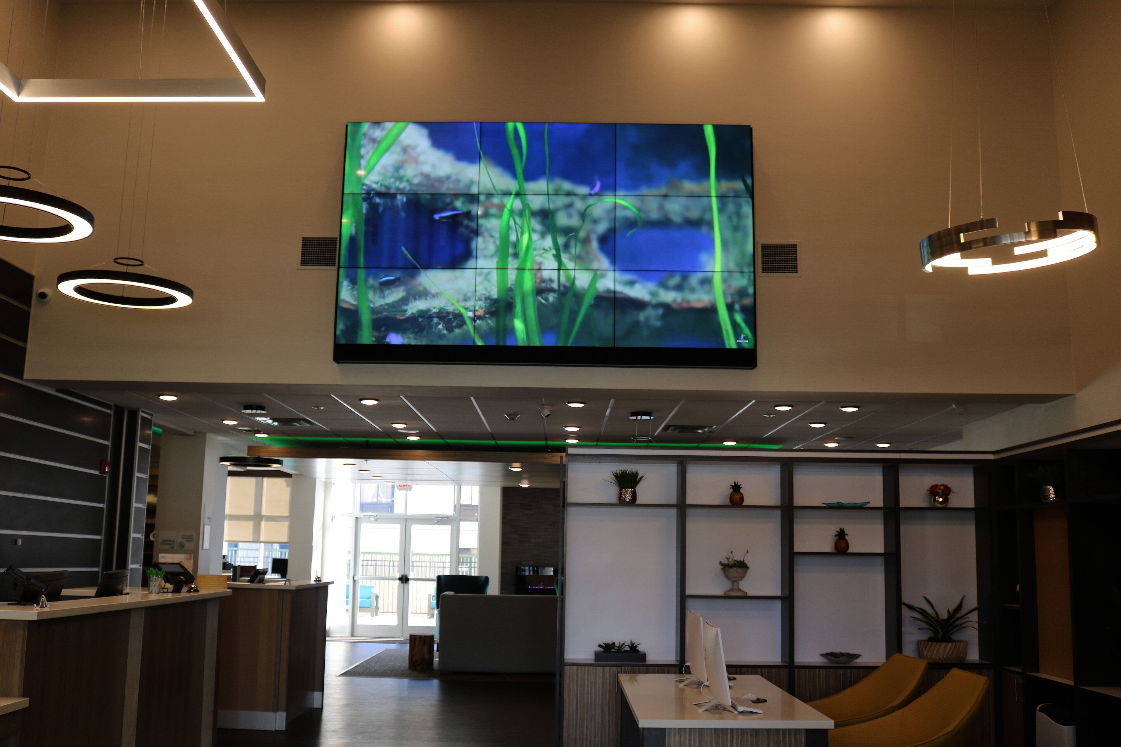 A modern lobby with a large digital display, a reception desk, seating area, and a reception counter.