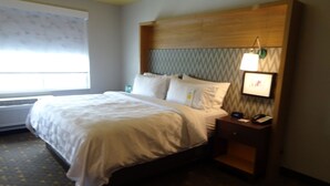 A hotel room with a bed, bedside table, lamp, and a window with blinds. - Holiday Inn Jonesboro by IHG (Jonesboro)