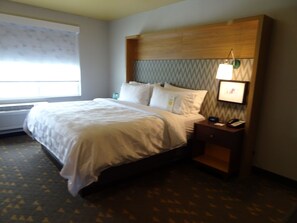 Une chambre d’hôtel avec un lit, une table de chevet, une lampe et une fenêtre avec des stores.