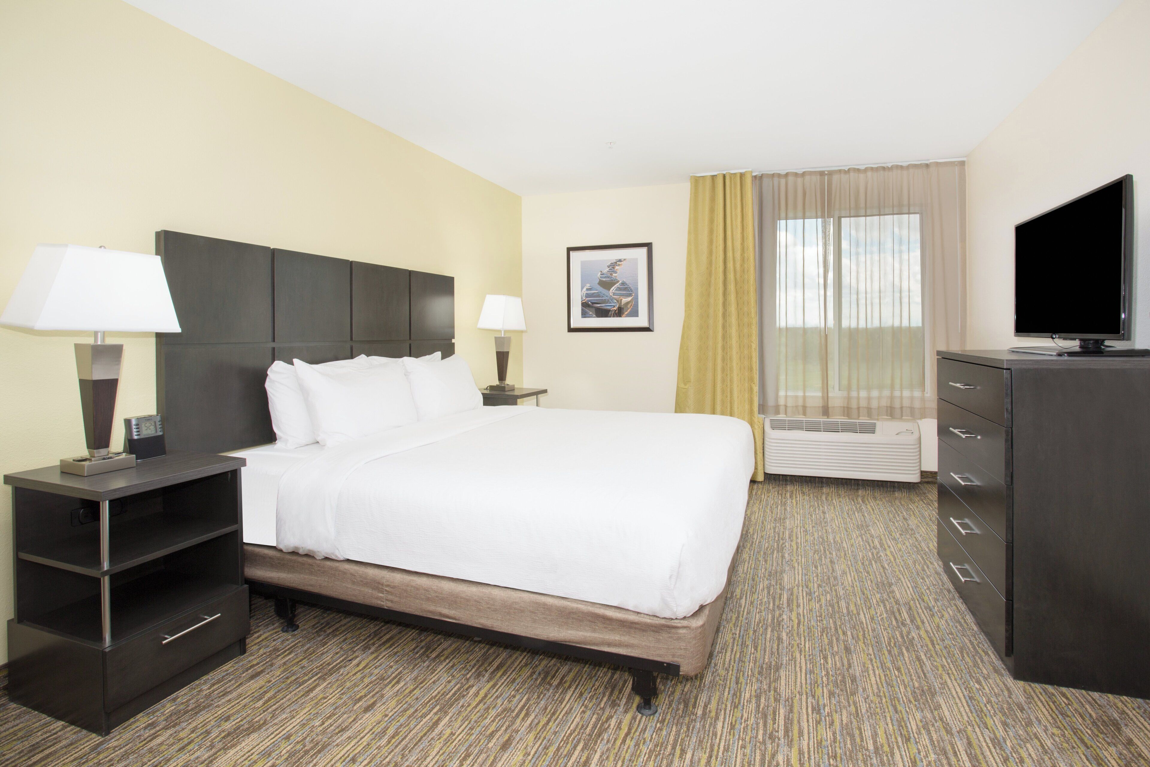 A hotel room with a bed, bedside tables, a TV, a heater, and a picture on the wall.