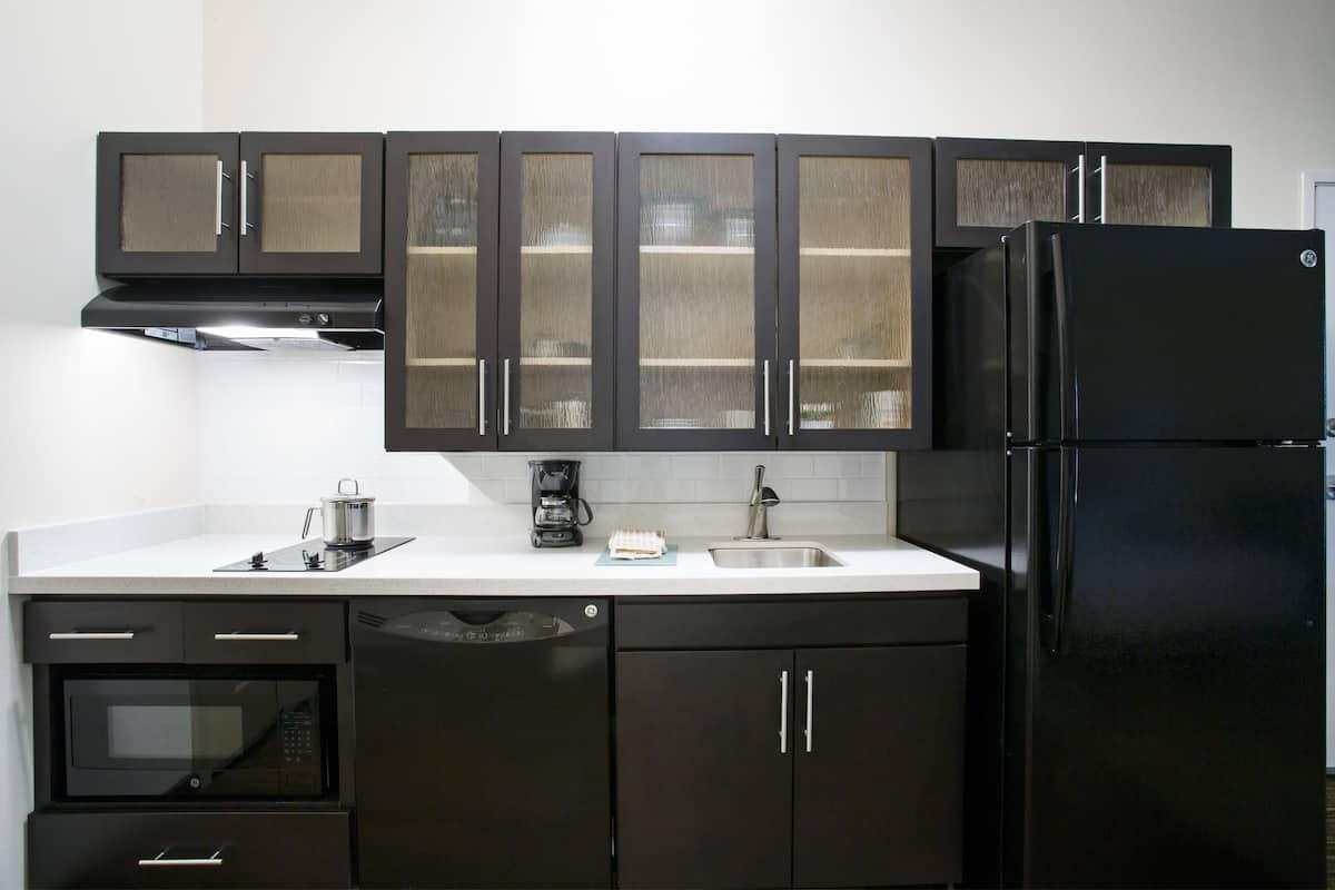 Una cocina con armarios oscuros, un refrigerador negro, un microondas y un lavavajillas.