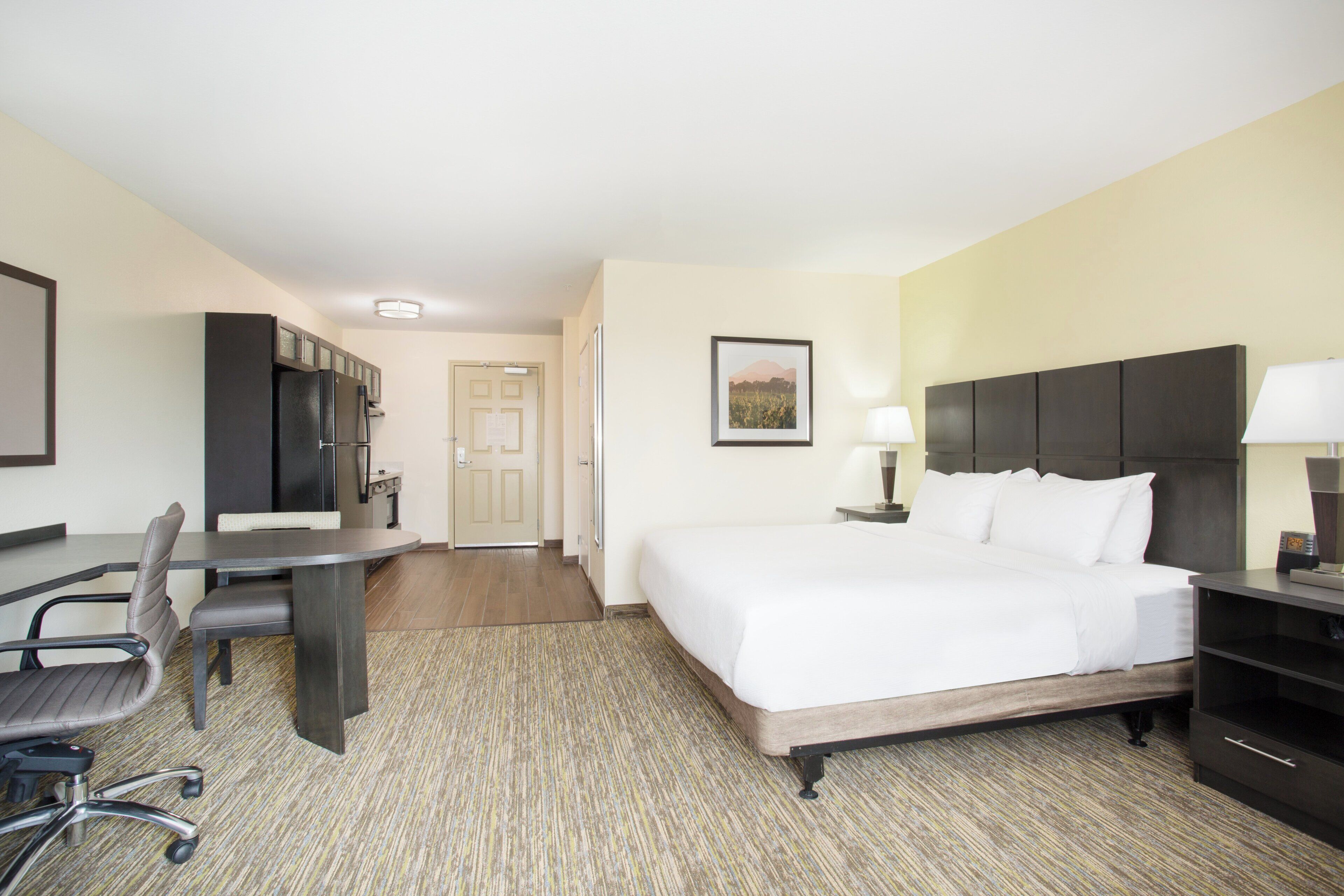 A hotel room with a bed, desk, chair, and a small kitchenette.