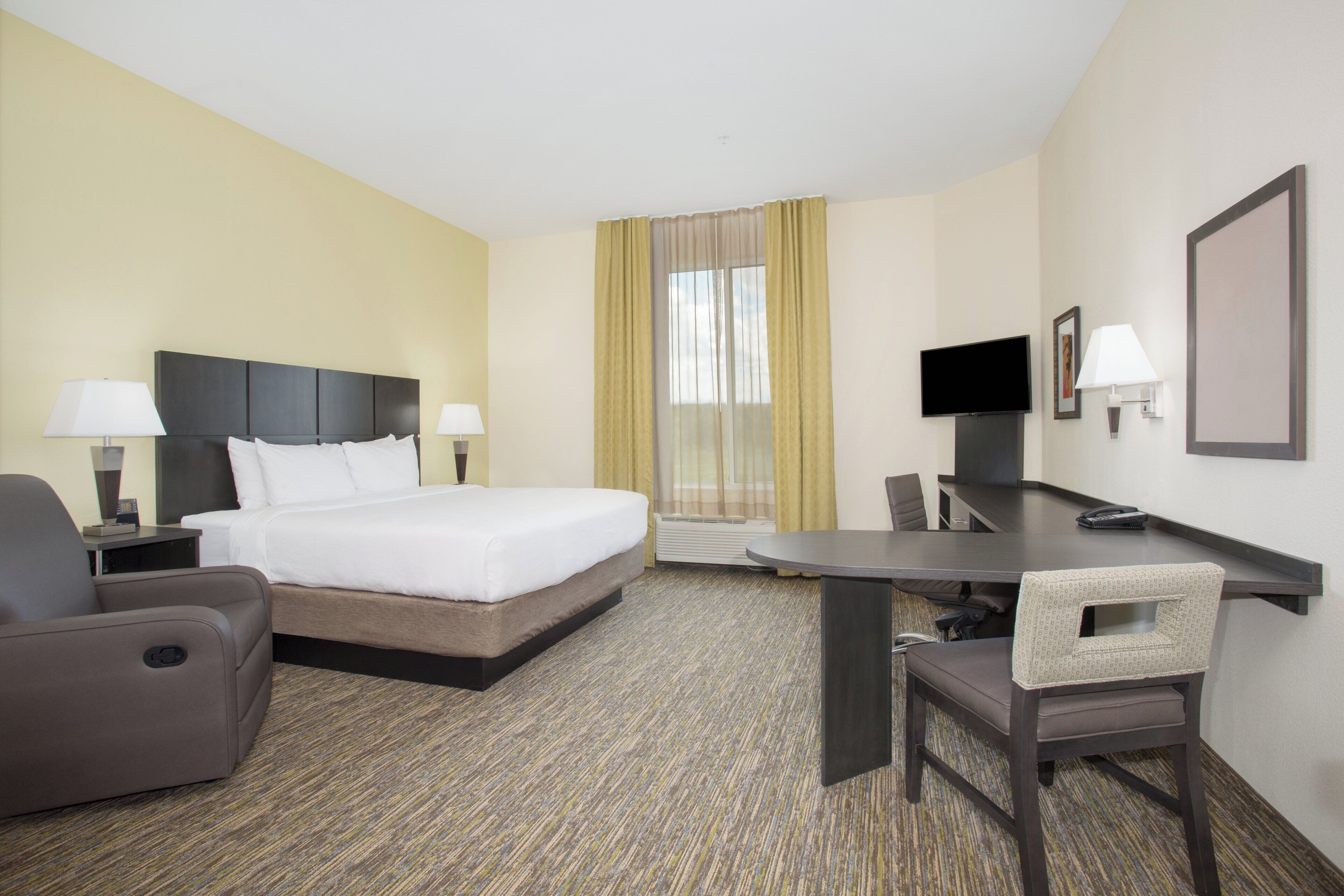 A hotel room with a bed, desk, chair, TV, and a window with curtains.