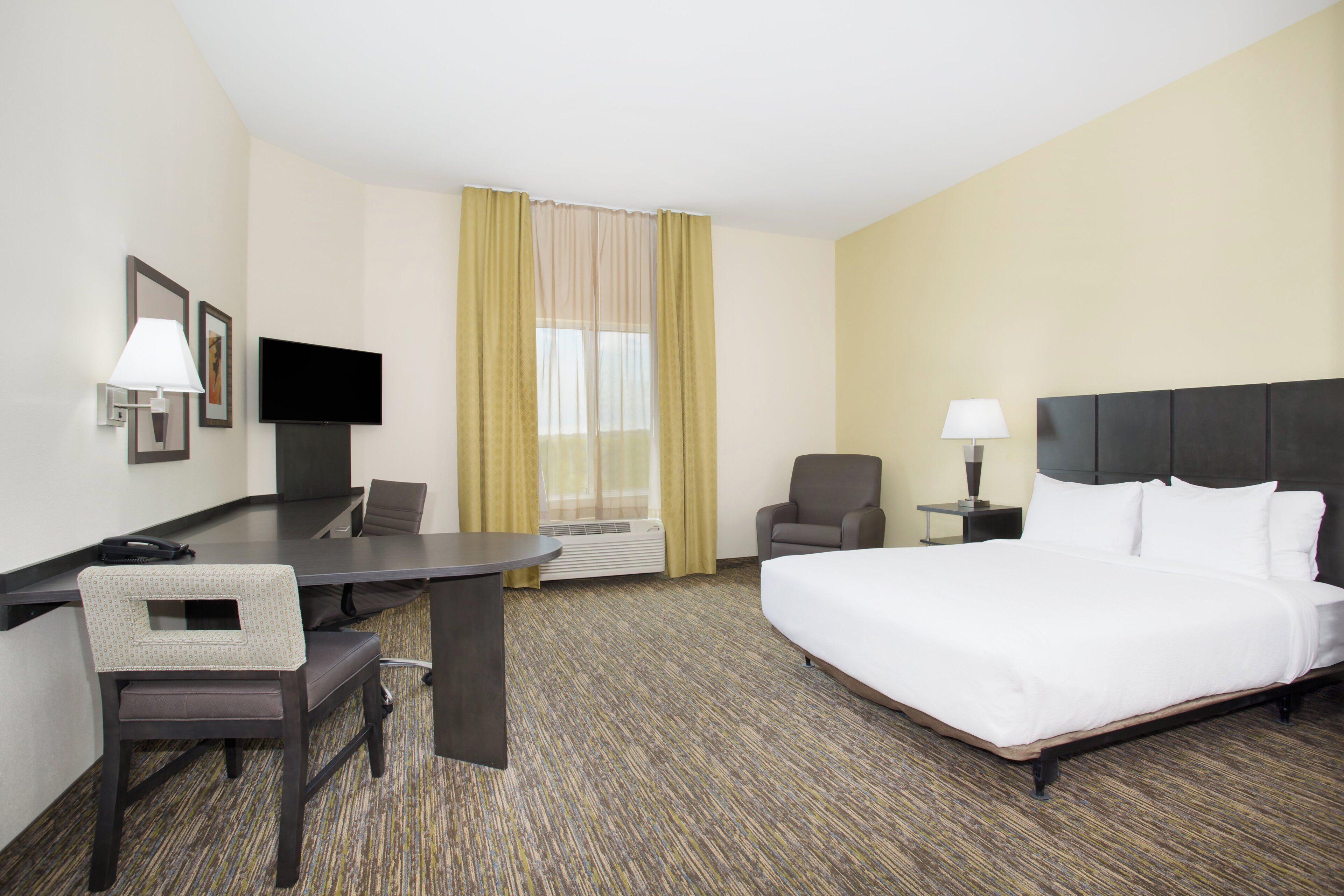 A hotel room with a bed, desk, chair, television, and a window with curtains.