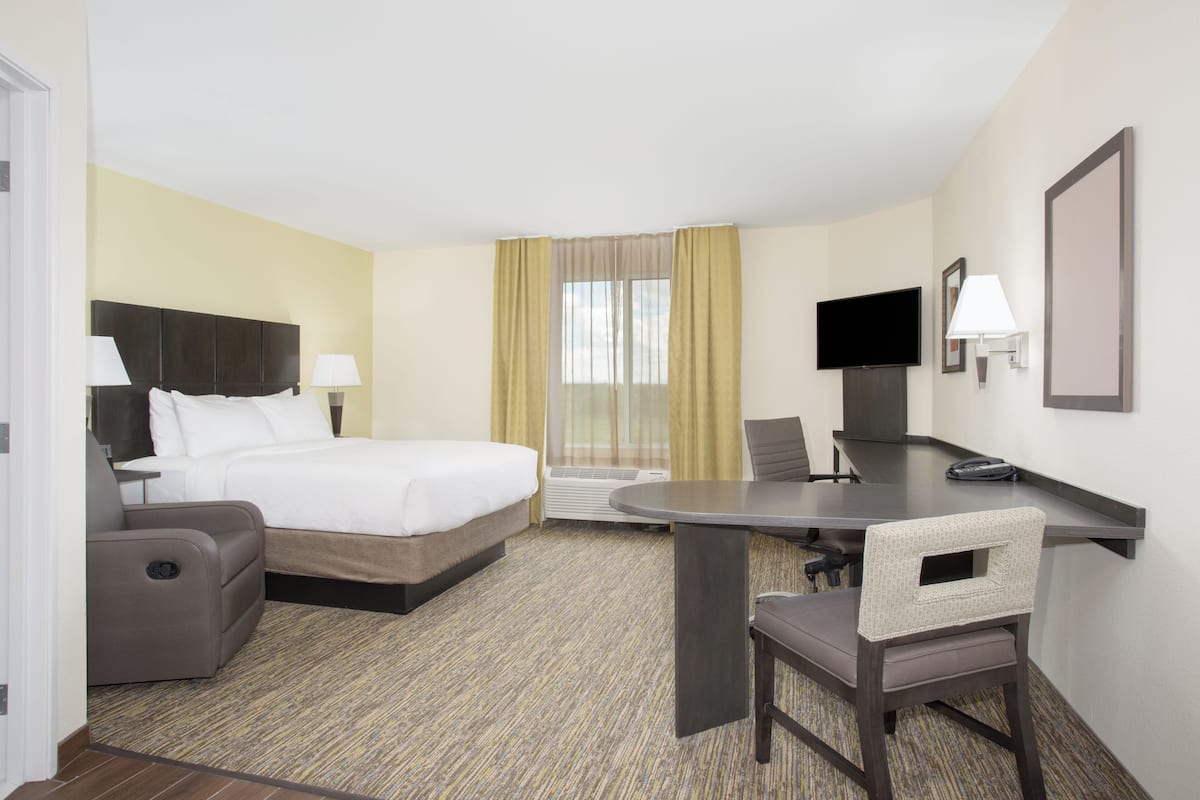 Habitación de hotel con cama, escritorio, silla, televisor y ventana con cortinas.